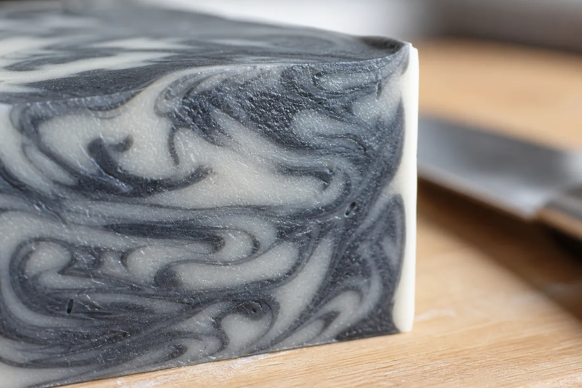 Mains gantées versant une pâte à savon colorée en vert dans un moule en bois chemisé