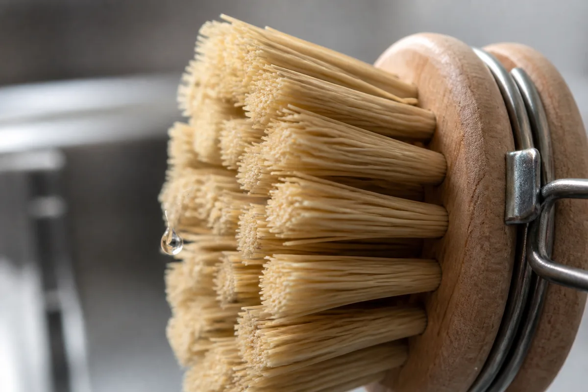 Brosse à vaisselle en bois clair posée sur un rebord d&rsquo;évier en inox