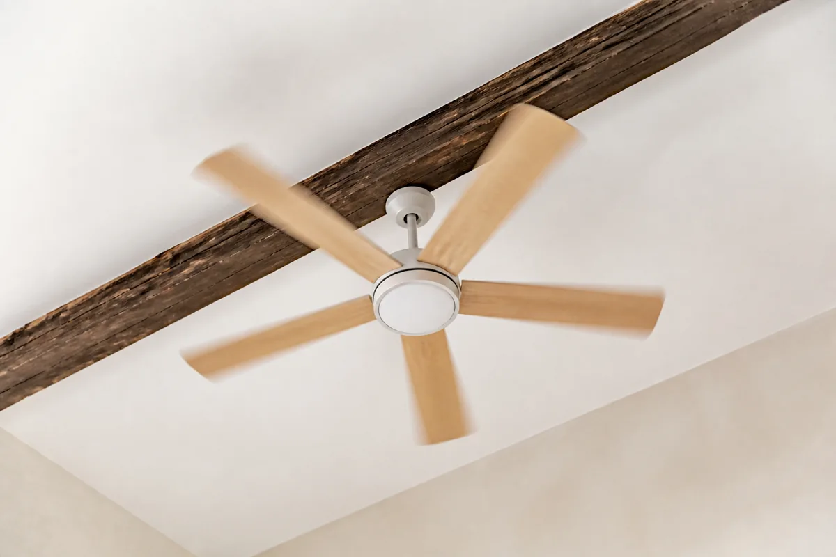 Ventilateur de plafond à pales en bois clair tournant dans une pièce aux murs chaulés